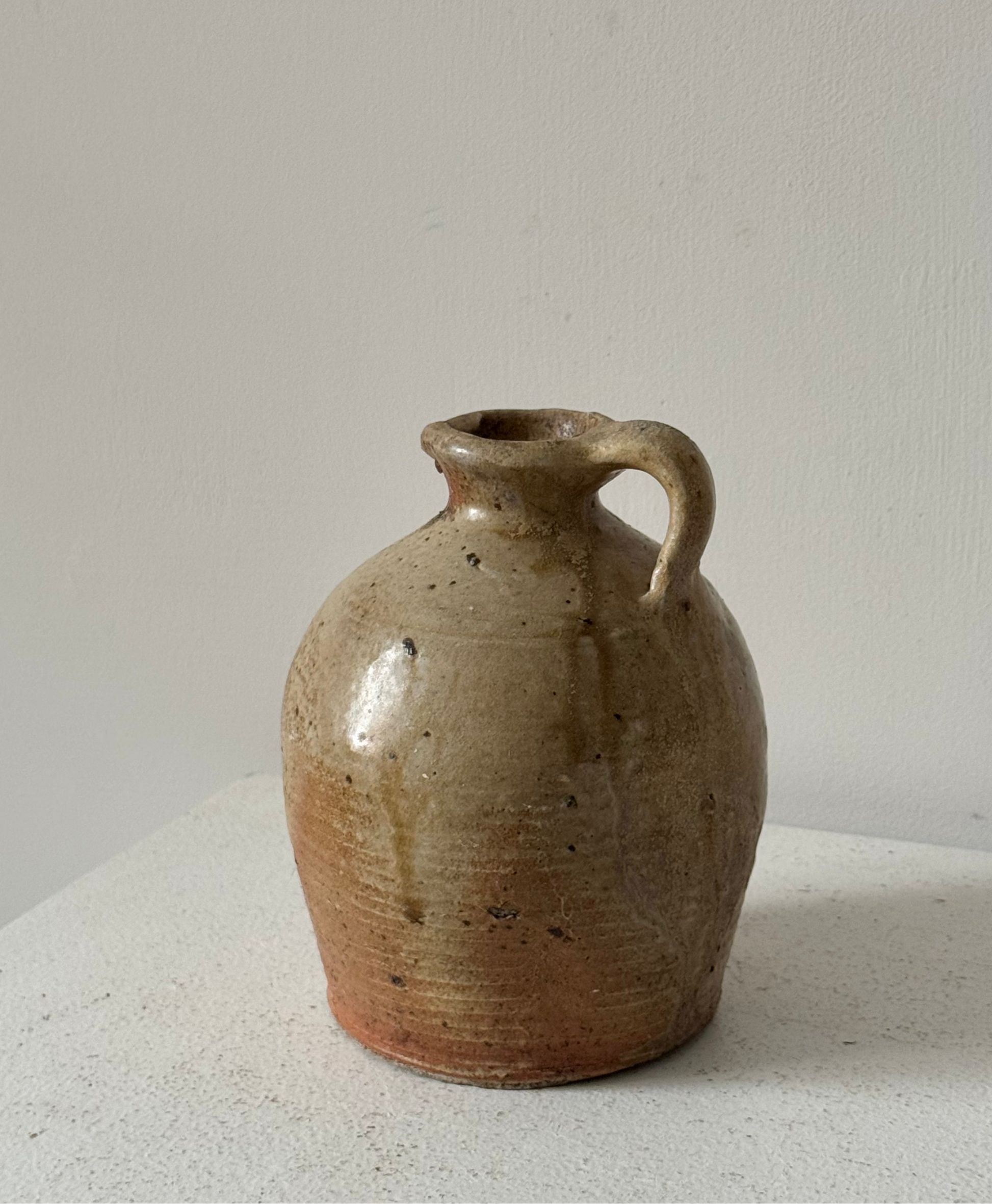 A rustic French Vintage jug with a rounded body, short handle, and wide flared rim, featuring a speckled earthy glaze in beige, brown, and terracotta tones, with prominent glaze drips.